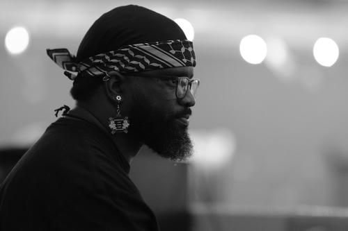 Profile photo of a Black person looking focused, wearing a
   striped bandana and a 'Nonbinary can look like anything' earring
