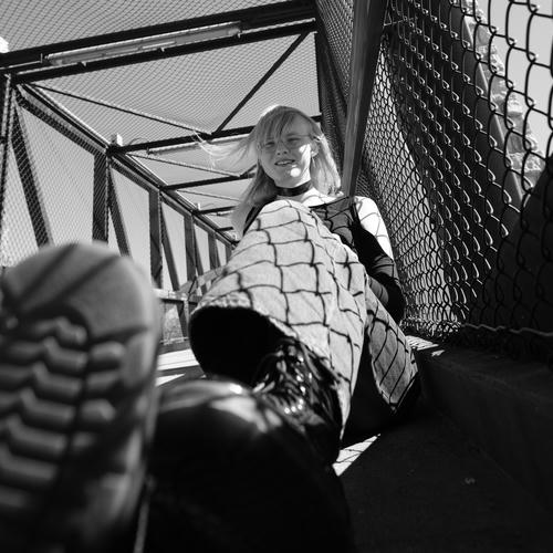 Black and white photograph of a young woman hanging out on a bridge,
  looking cool.